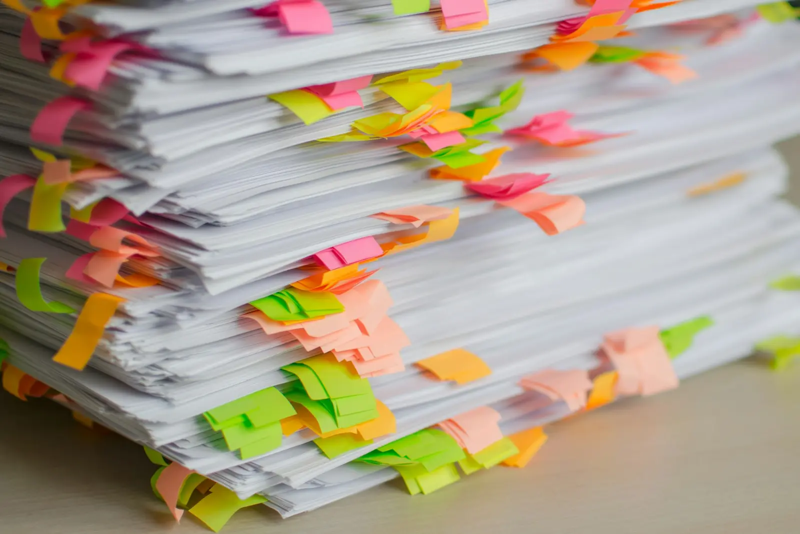 A tall stack of printed pages with dozens of pink, orange, yellow and green sticky tabs marking places in it