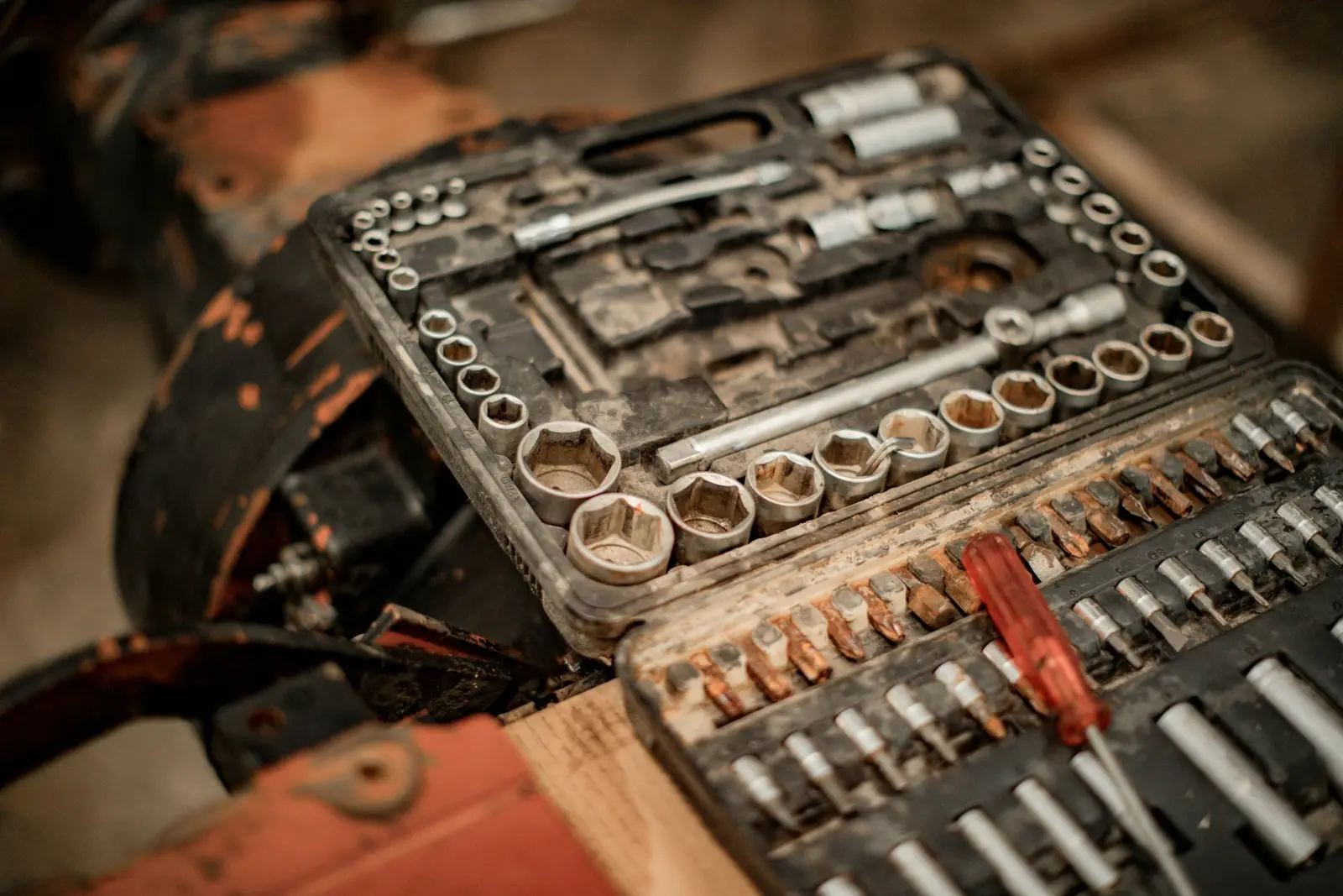 An open, well-worn case of socket wrenches and screwdriver bits, each piece set in its own slot, with a red-handled screwdriver across it