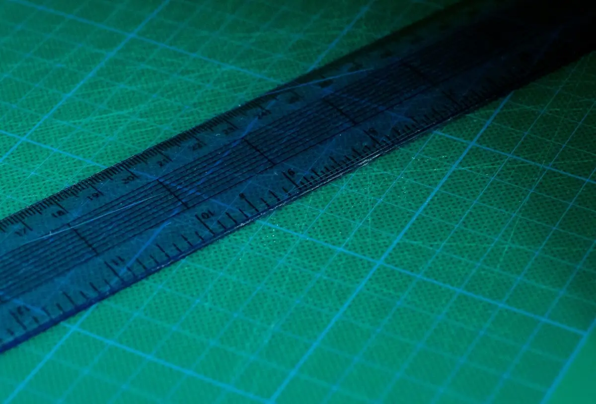 A clear blue ruler lying diagonally across a green cutting mat printed with a measuring grid