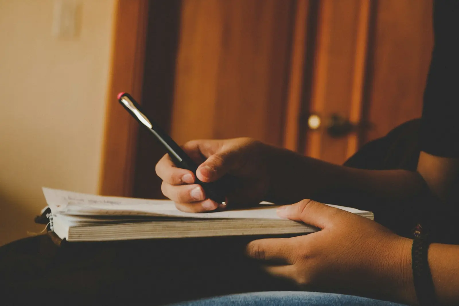 A person writing in an open spiral notebook resting on their lap