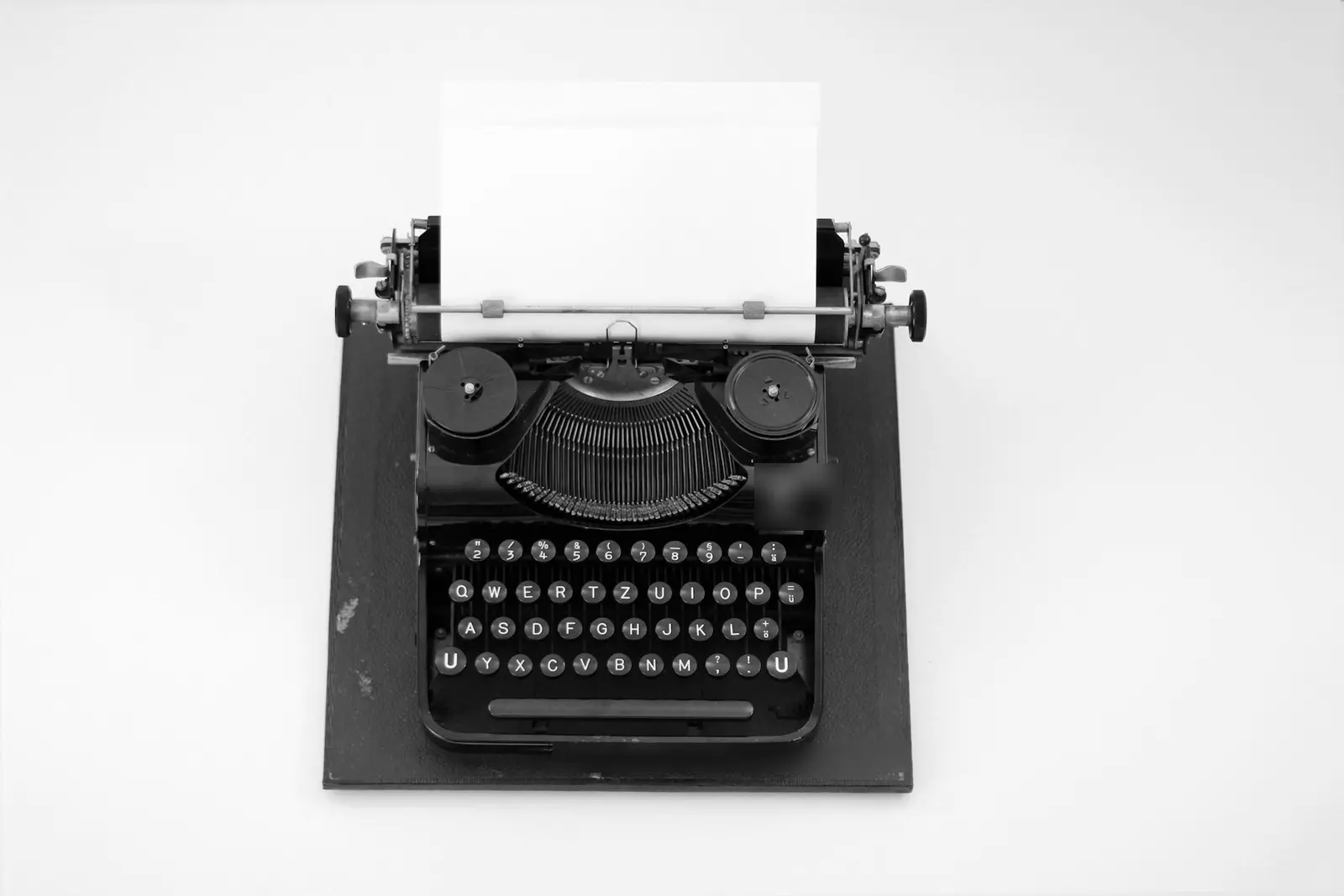 A black vintage typewriter seen from above on a dark board, with a blank sheet of paper loaded in it