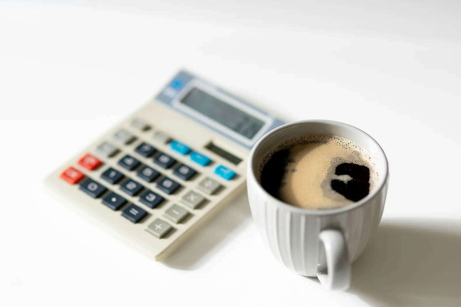 A desk calculator next to a cup of black coffee on a white table