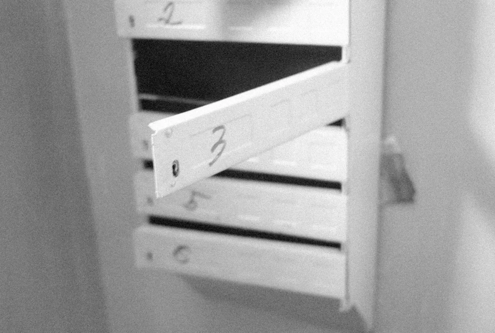 Black and white close-up of a stack of white numbered drawers, one front hanging open at an angle with a handwritten 3 on it