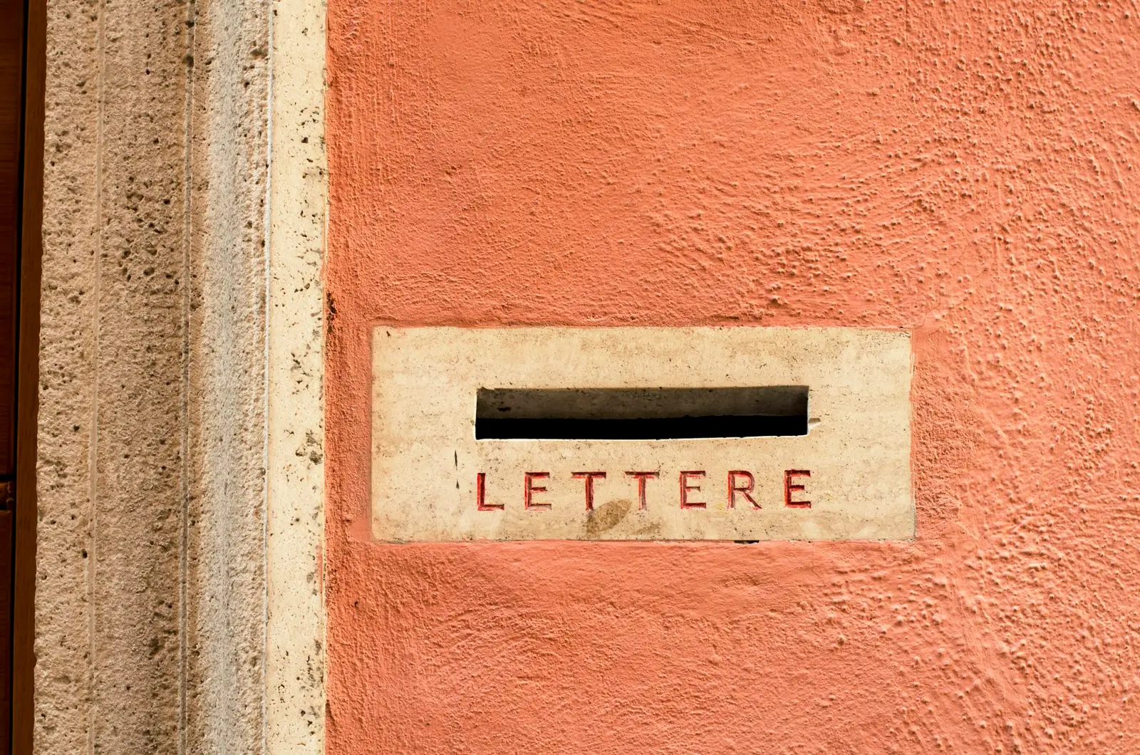 A letter slot set into an orange wall, framed in stone with the word LETTERE carved beneath the opening