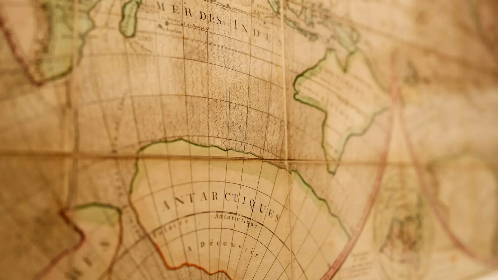 A close-up of an antique world map in warm brown tones, with curved grid lines and old French place labels