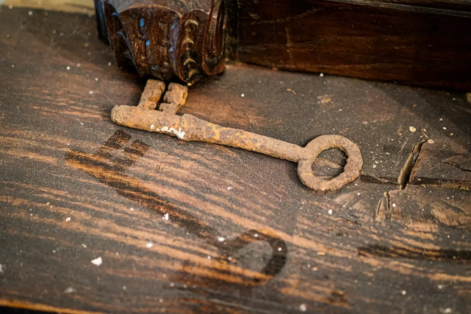 An old rusty key lying on a scratched dark wooden table