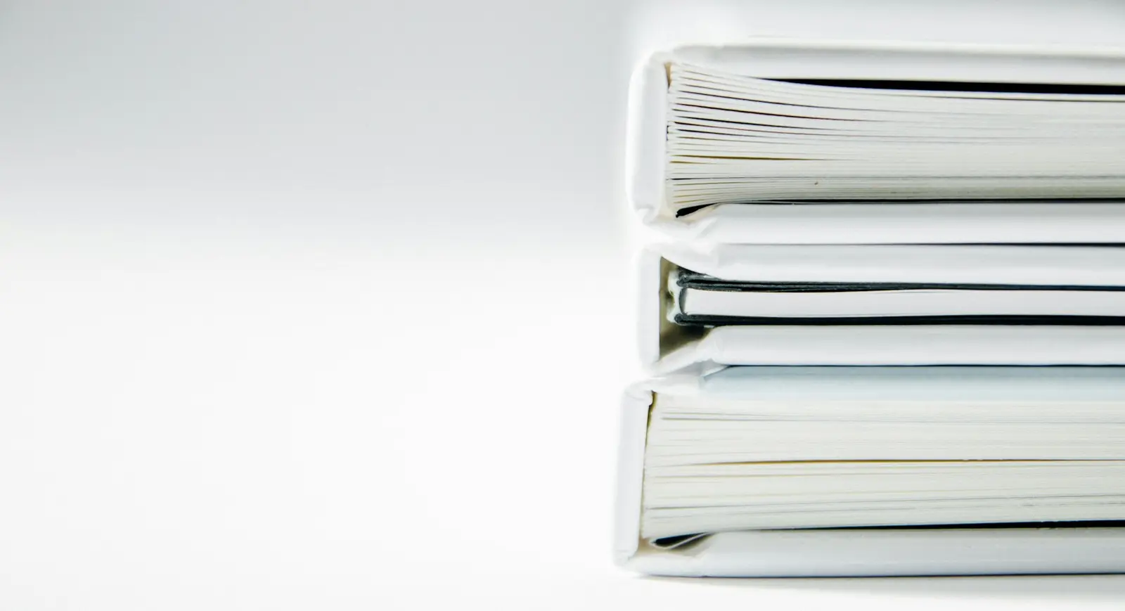 A stack of thick white ring binders seen from the side, on a plain white surface