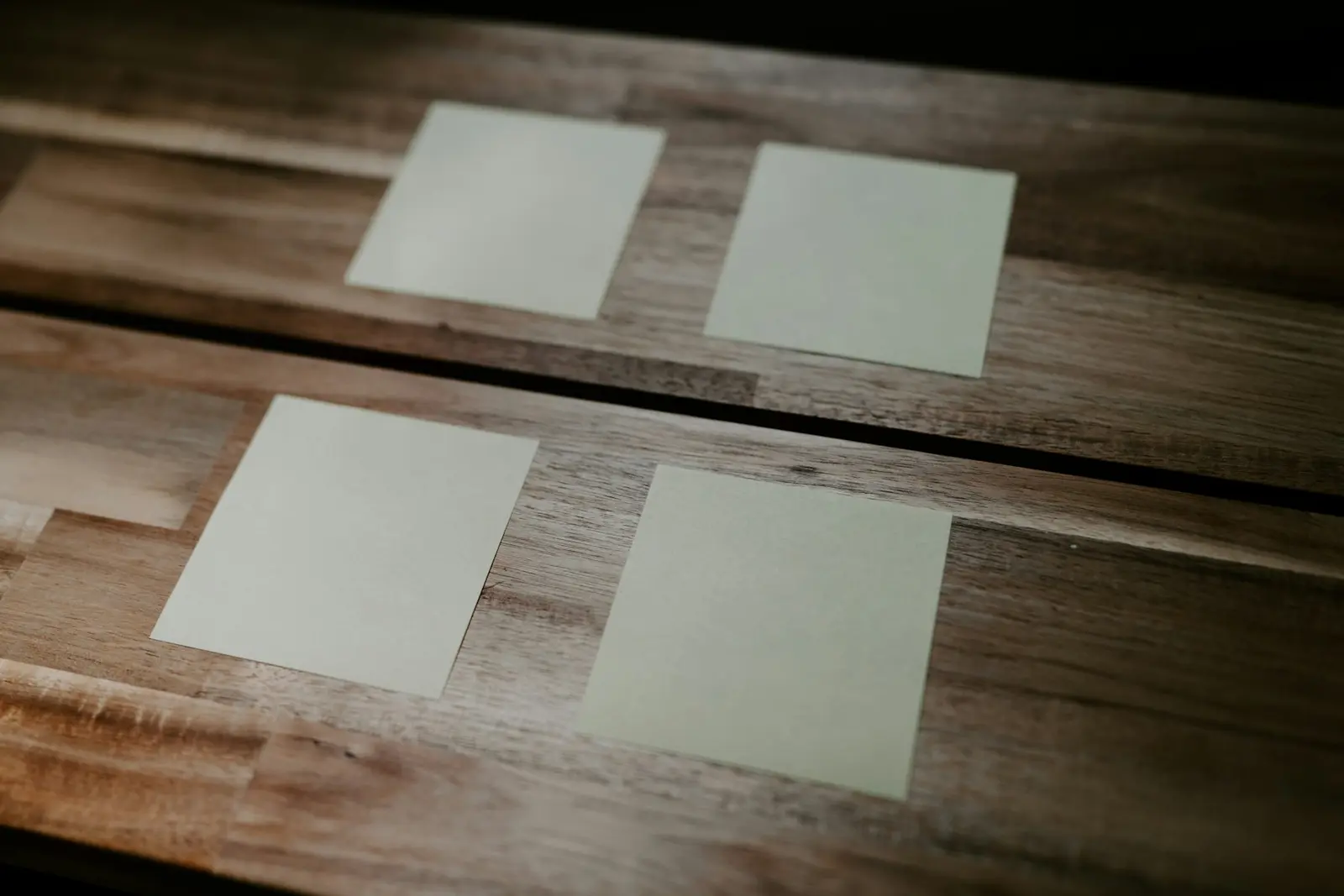 Four blank pale green paper cards laid out in two rows on a wooden table