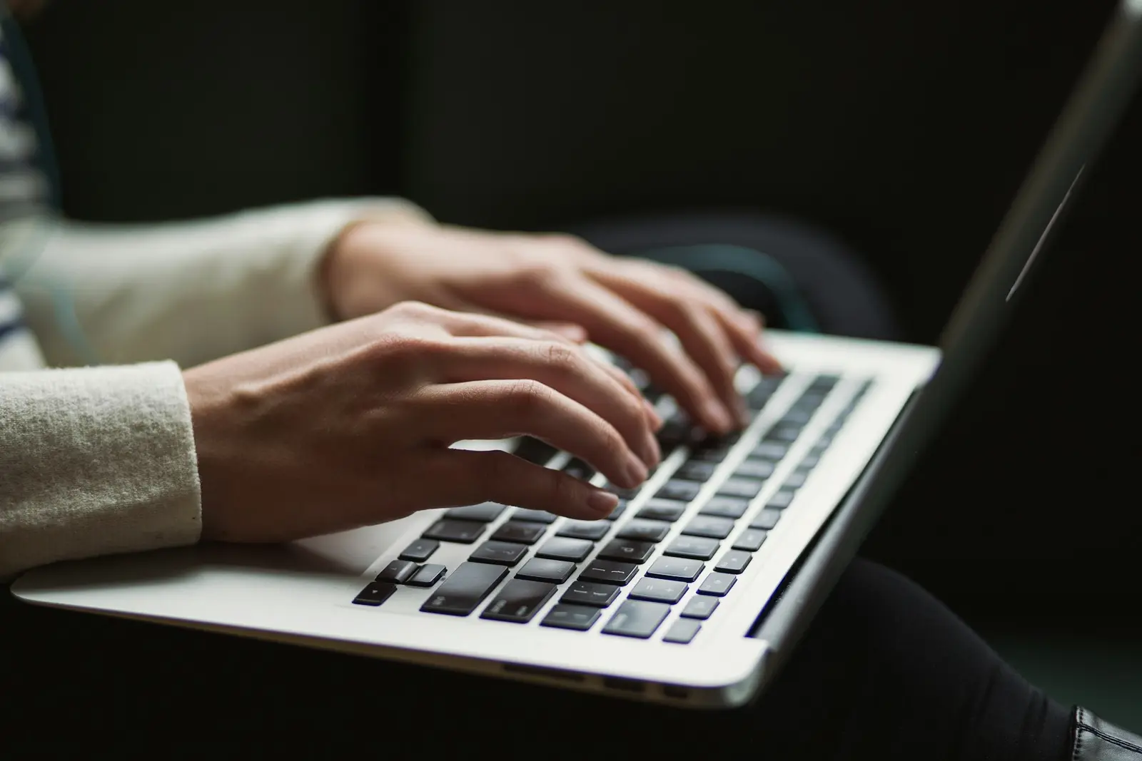 Two hands typing on a silver laptop keyboard in a dim room