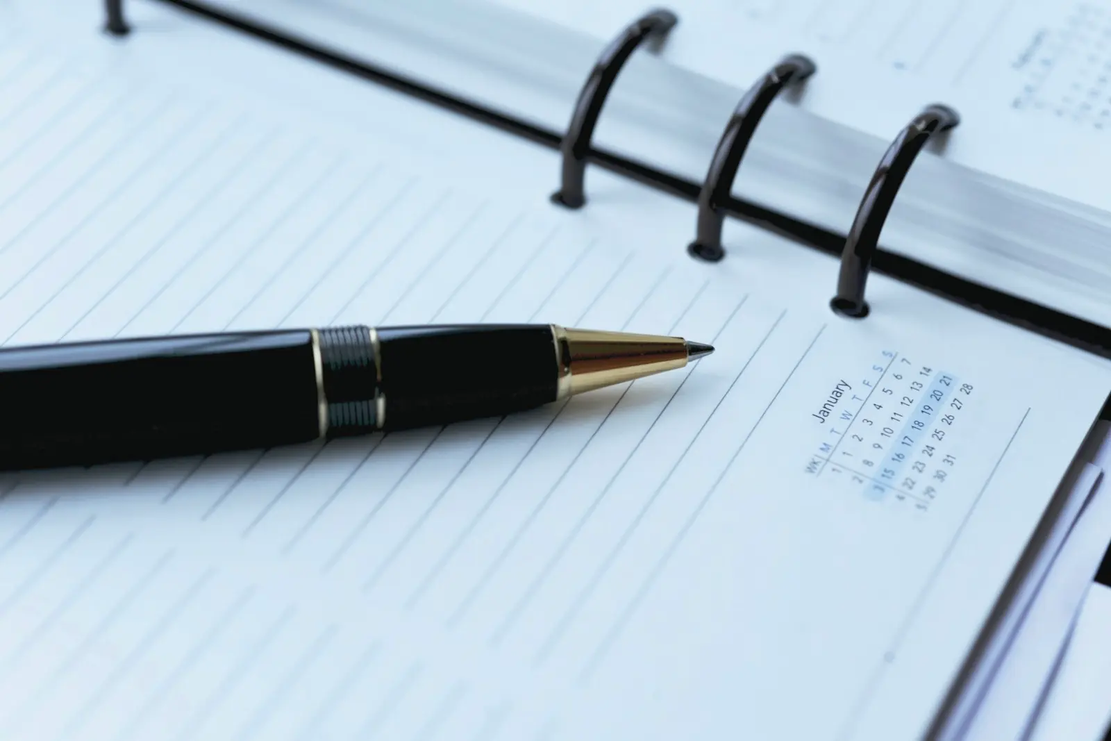A black pen lying across an open ring-bound diary ruled in lines, with a small printed January calendar on the right-hand page