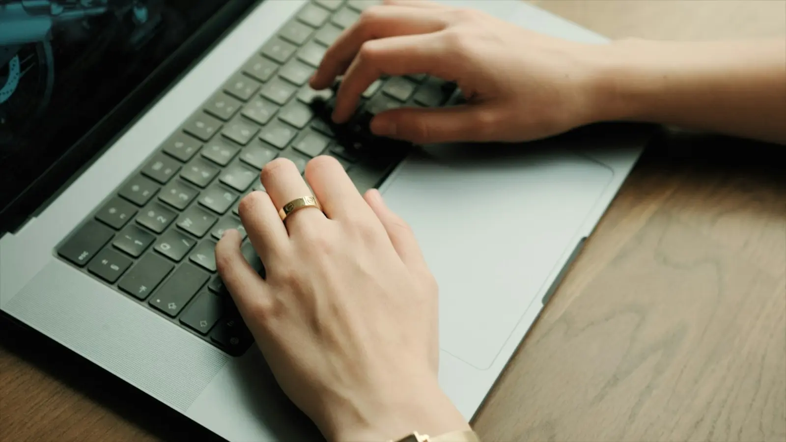 Two hands typing on a silver laptop keyboard resting on a wooden table, seen from above
