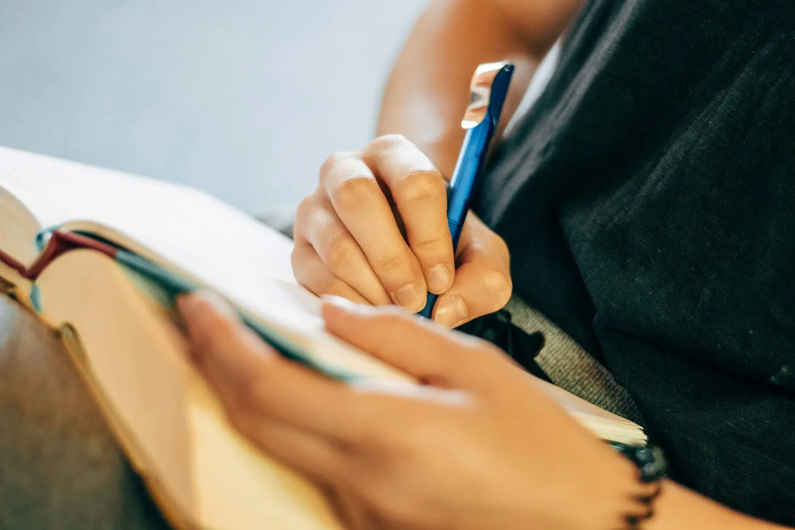 A hand writing in an open notebook with a dark blue pen while the other hand holds the pages flat