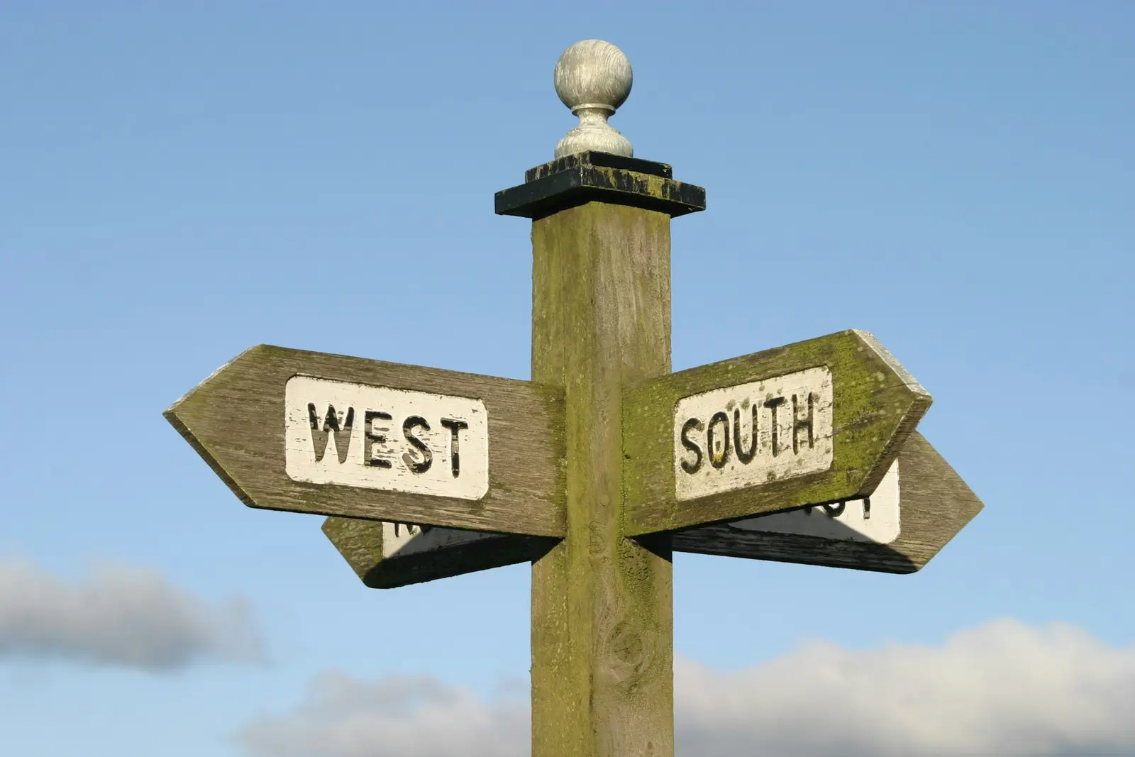 A weathered wooden signpost against a blue sky, with arms reading West and South pointing in opposite directions and two more arms partly hidden behind them