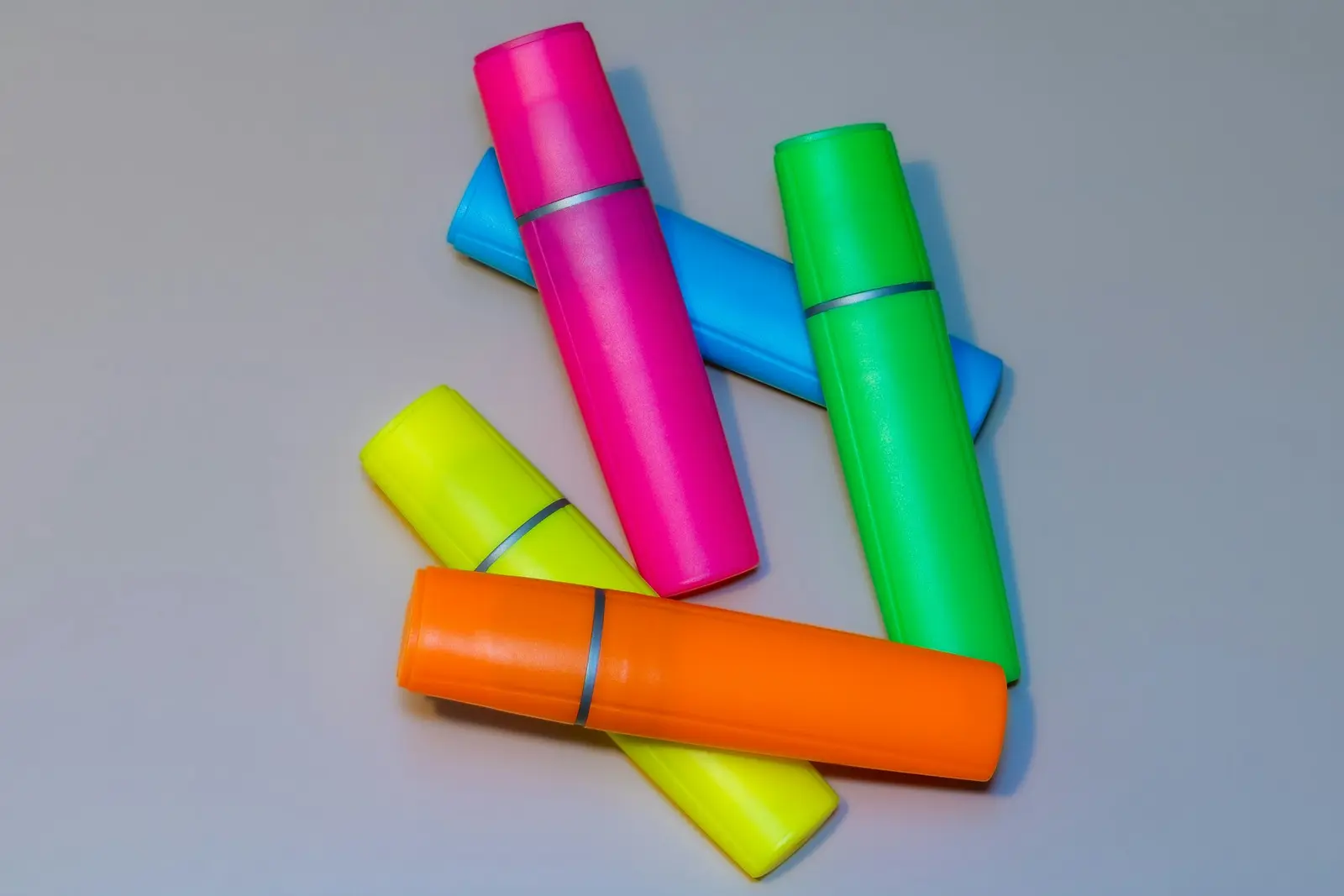Five highlighter pens in pink, blue, green, yellow and orange lying on a grey surface