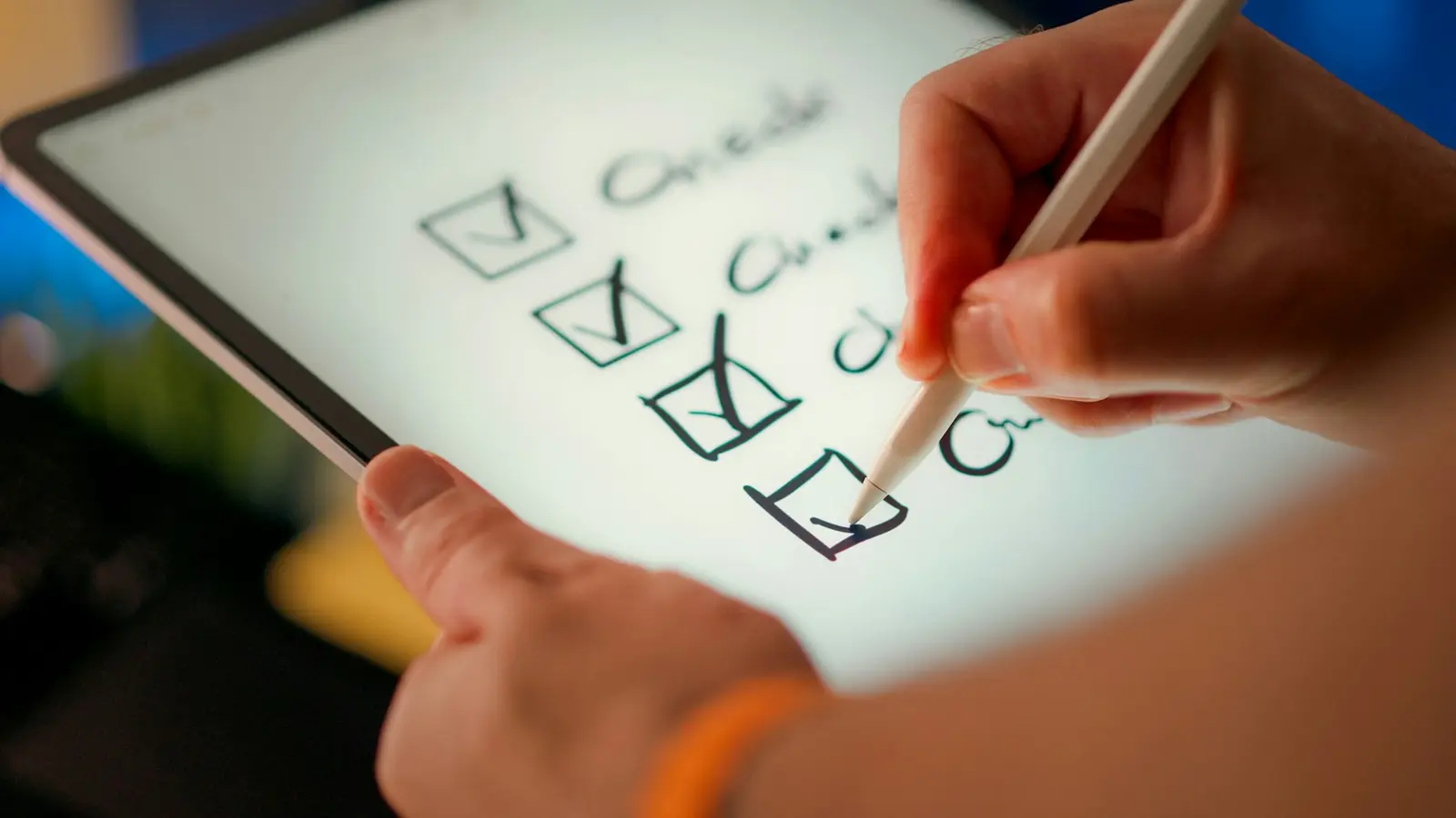 A hand holding a stylus ticks the last of four boxes in a handwritten checklist on a tablet screen